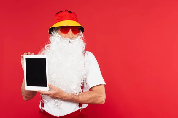 Bärtiger Weihnachtsmann mit Sonnenbrille und digitalem Tablet mit leerem Bildschirm auf rotem Hintergrund — Stockfoto