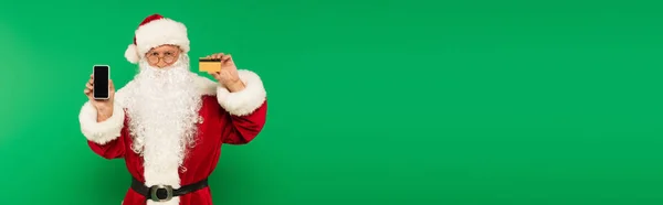 Father christmas holding smartphone and credit card isolated on green, banner — Stock Photo