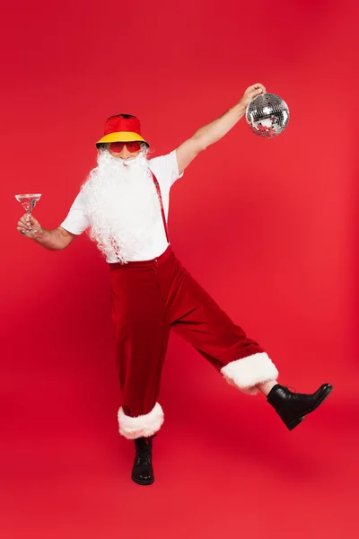 Santa claus dans des lunettes de soleil tenant boule disco et cocktail sur fond rouge — Photo de stock