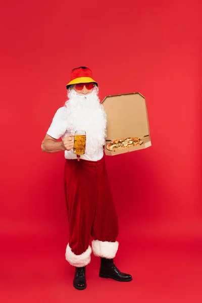 Father christmas in sunglasses holding mug of beer and pizza on red background — Stock Photo