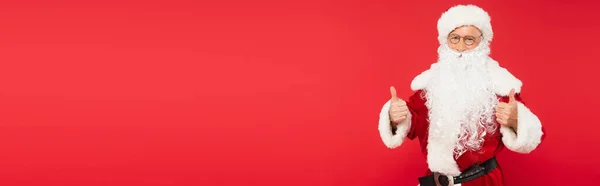 Santa claus in eyeglasses showing thumbs up isolated on red, banner — Stock Photo