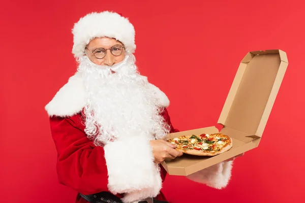 Santa claus in eyeglasses and hat holding pizza in box isolated on red — Stock Photo