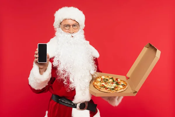 Santa claus showing smartphone with blank screen and holding pizza in box isolated on red — Stock Photo