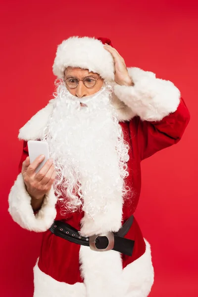 Worried santa claus using smartphone isolated on red — Stock Photo