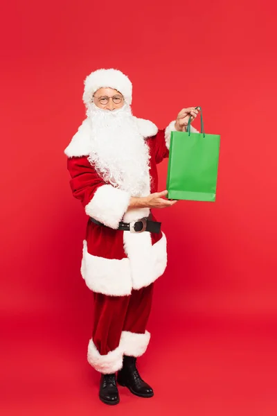 Santa Claus en traje sosteniendo bolsa de compras sobre fondo rojo - foto de stock