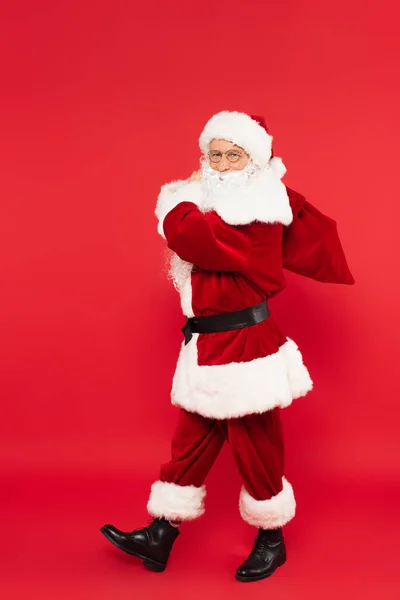 Père Noël avec sac marchant sur fond rouge — Photo de stock