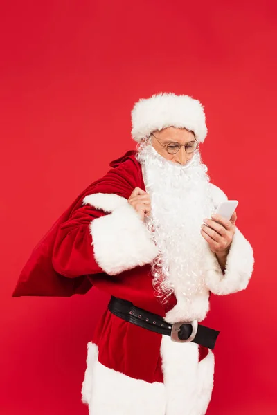 Santa Claus con saco usando teléfono móvil aislado en rojo - foto de stock