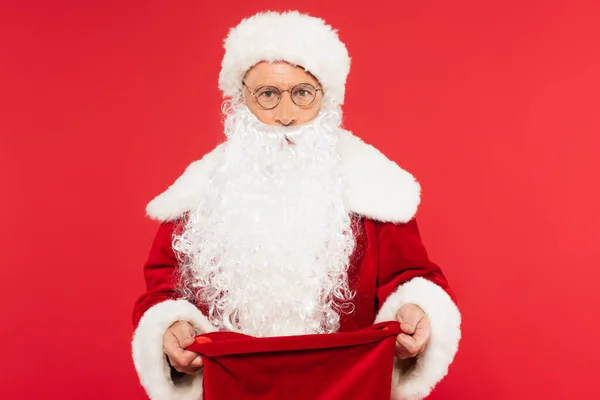 Santa Claus con saco abierto mirando a la cámara aislada en rojo - foto de stock