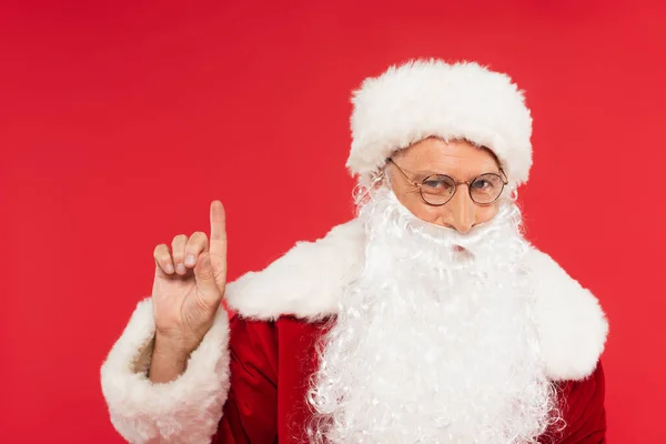 Santa claus in hat pointing with finger isolated on red — Stock Photo