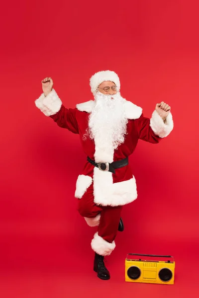 Santa claus bailando cerca de boombox sobre fondo rojo - foto de stock