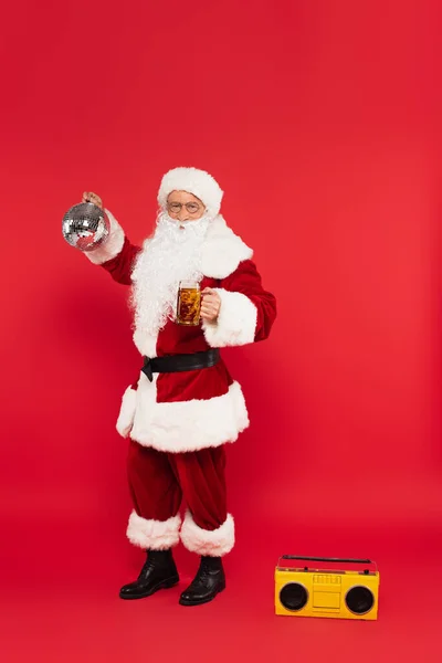 Santa Claude avec bière et boule disco debout près de boombox sur fond rouge — Photo de stock