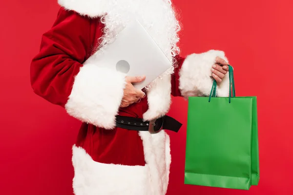 Ausgeschnittene Ansicht des Weihnachtsmannes mit Einkaufstaschen und Laptop isoliert auf Rot — Stockfoto