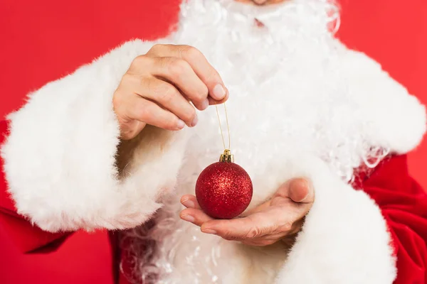 Vue recadrée du Père Noël flou tenant la boule de Noël isolée sur rouge — Photo de stock