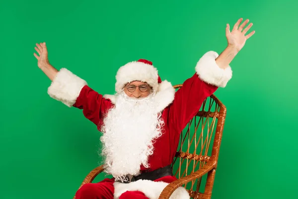 Збуджений Санта Клаус сидить на кріслі, ізольованому на зеленому — стокове фото