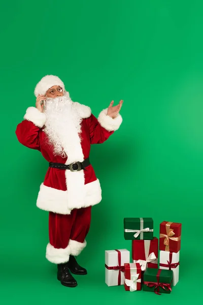 Santa claus talking on smartphone near presents on green background — Stock Photo