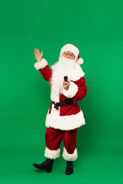 Santa Claus en traje sosteniendo micrófono y apuntando al fondo verde - foto de stock