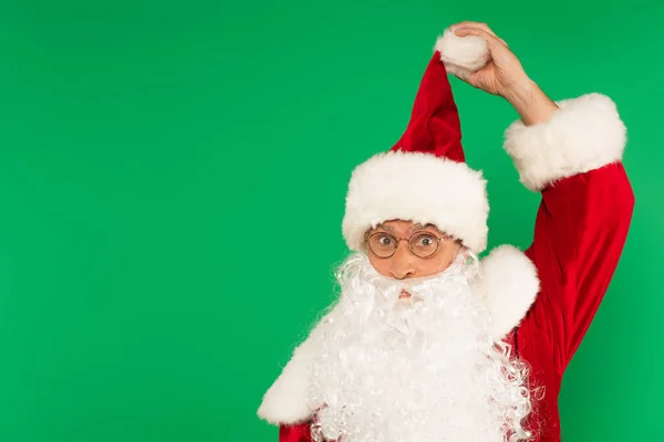 Bearded santa claus in eyeglasses holding hat isolated on green — Stock Photo