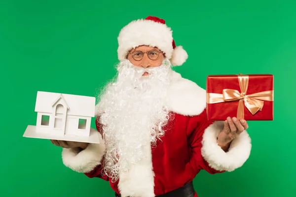 Santa claus tenant modèle de maison et cadeau isolé sur vert — Photo de stock