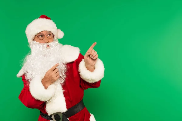 Père Noël en chapeau et costume pointant avec les doigts isolés sur vert — Photo de stock