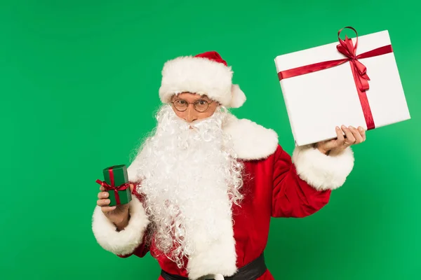 Санта-Клаус держит подарки и смотрит на камеру, изолированную на зеленый — стоковое фото