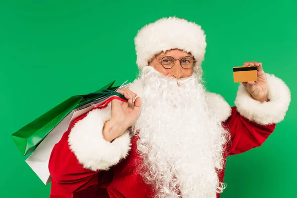 Santa Claude avec sacs à provisions et carte de crédit regardant la caméra isolée sur vert — Photo de stock