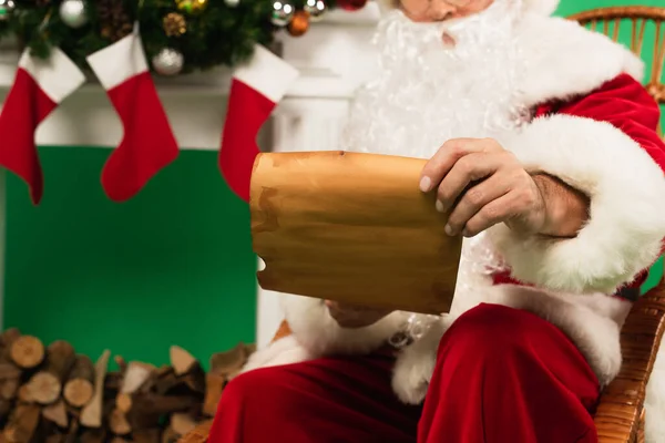 Vista cortada de papel de Pai Natal desfocado perto da lareira no fundo verde — Fotografia de Stock