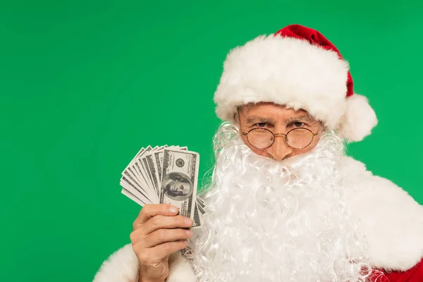 Père Noël dans les lunettes regardant la caméra et tenant des dollars isolés sur vert — Photo de stock