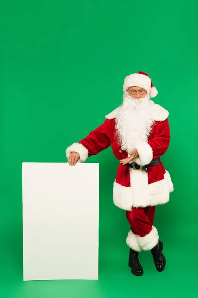 Santa claus pointing at white placard on green background — Stock Photo