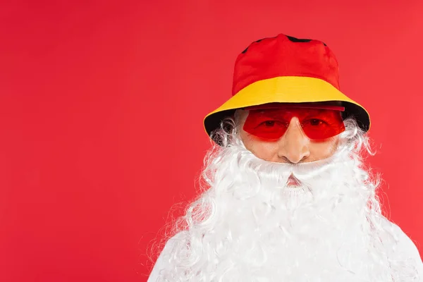 Santa claus in sunglasses and panama looking at camera isolated on red — Stock Photo