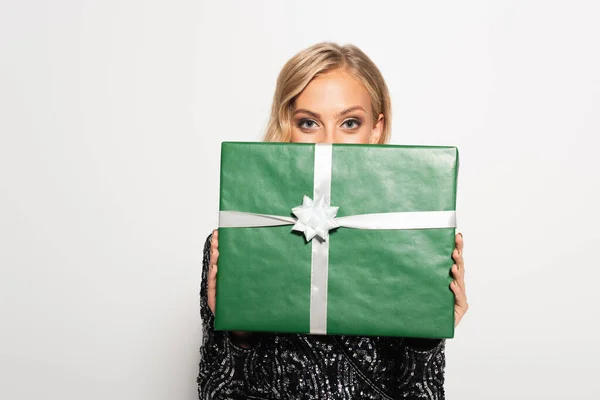 Junge blonde Frau versteckt Gesicht hinter grünem Geschenkkarton, während sie isoliert auf weiß in die Kamera schaut — Stockfoto