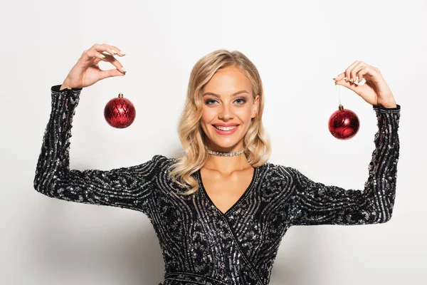 Mujer alegre y elegante sonriendo y mostrando bolas de Navidad en blanco - foto de stock