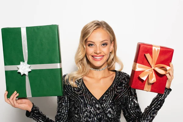 Mujer sonriente en blusa negra y brillante mostrando cajas de regalo rojas y verdes en blanco - foto de stock