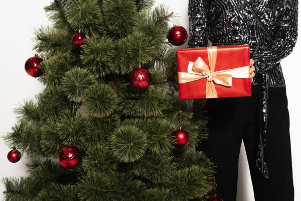 Partial view of elegant woman holding red gift box near christmas tree on white — Stock Photo