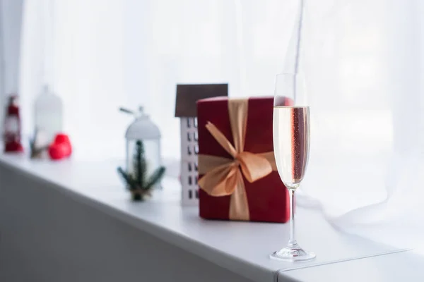 Enfoque selectivo de la caja de regalo roja cerca del modelo de casa decorativa borrosa en el alféizar de la ventana - foto de stock