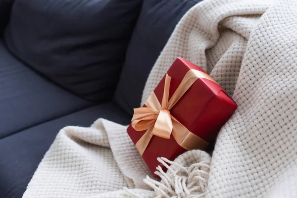 Divano con morbida coperta e confezione regalo rossa decorata con nastro — Foto stock