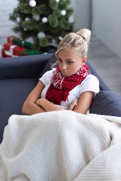 Vista ad alto angolo di donna malata e sconvolta con braccia incrociate sul divano vicino all'albero di Natale su sfondo sfocato — Foto stock