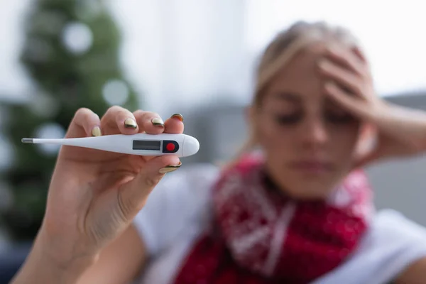 Selective focus of electronic thermometer in hand of sick woman on blurred background — Stock Photo