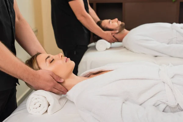 Masseur macht Nackenmassage für junge Frau im Bademantel in der Nähe von Kollegen und Mann im Wellnesszentrum — Stockfoto