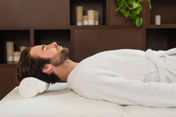 Side view of man in bathrobe lying on massage table in spa center — Stock Photo