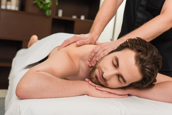 Young man lying on massage table near masseur in spa center — Stock Photo