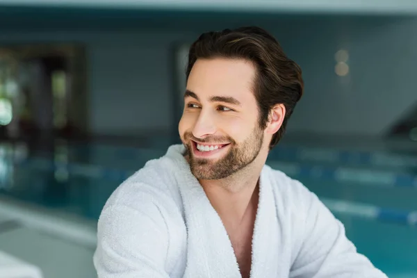 Cheerful man in white bathrobe looking away in spa center — Stock Photo