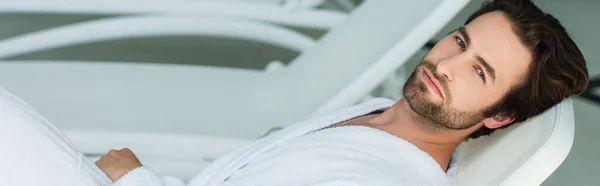 Mann im weißen Bademantel blickt auf Liegestuhl im Wellness-Center in die Kamera, Banner — Stockfoto