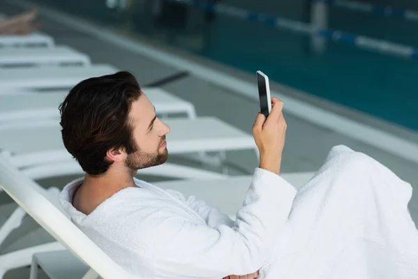 Vue latérale de l'homme en peignoir en utilisant smartphone dans le centre de spa — Photo de stock