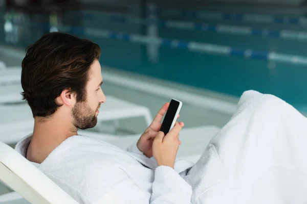 Side view of man using cellphone on deck chair in spa center — Stock Photo