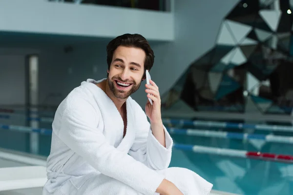 Sorrindo homem em roupão de banho falando no smartphone no centro de spa — Fotografia de Stock