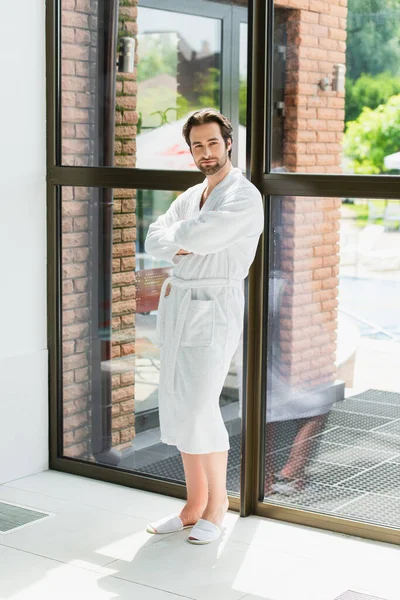 Young man in white bathrobe standing near window in spa center — Stock Photo