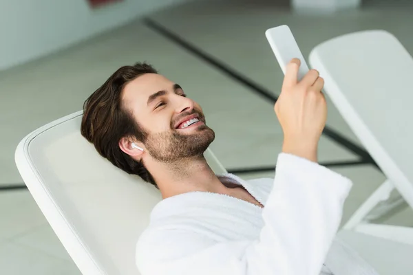 Smiling man in earphone using smartphone in spa center — Stock Photo