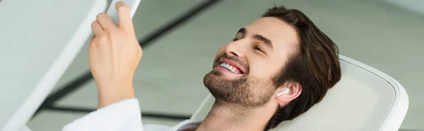 Fröhlicher Mann mit drahtlosem Kopfhörer per Smartphone im Wellness-Center, Banner — Stockfoto