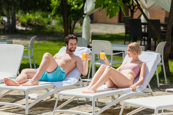 Giovane coppia positiva che tiene succo d'arancia sulle sedie a sdraio sul resort — Foto stock