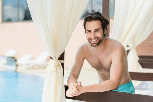 Smiling man in swimming trunks standing near lounge bed on resort — Stock Photo